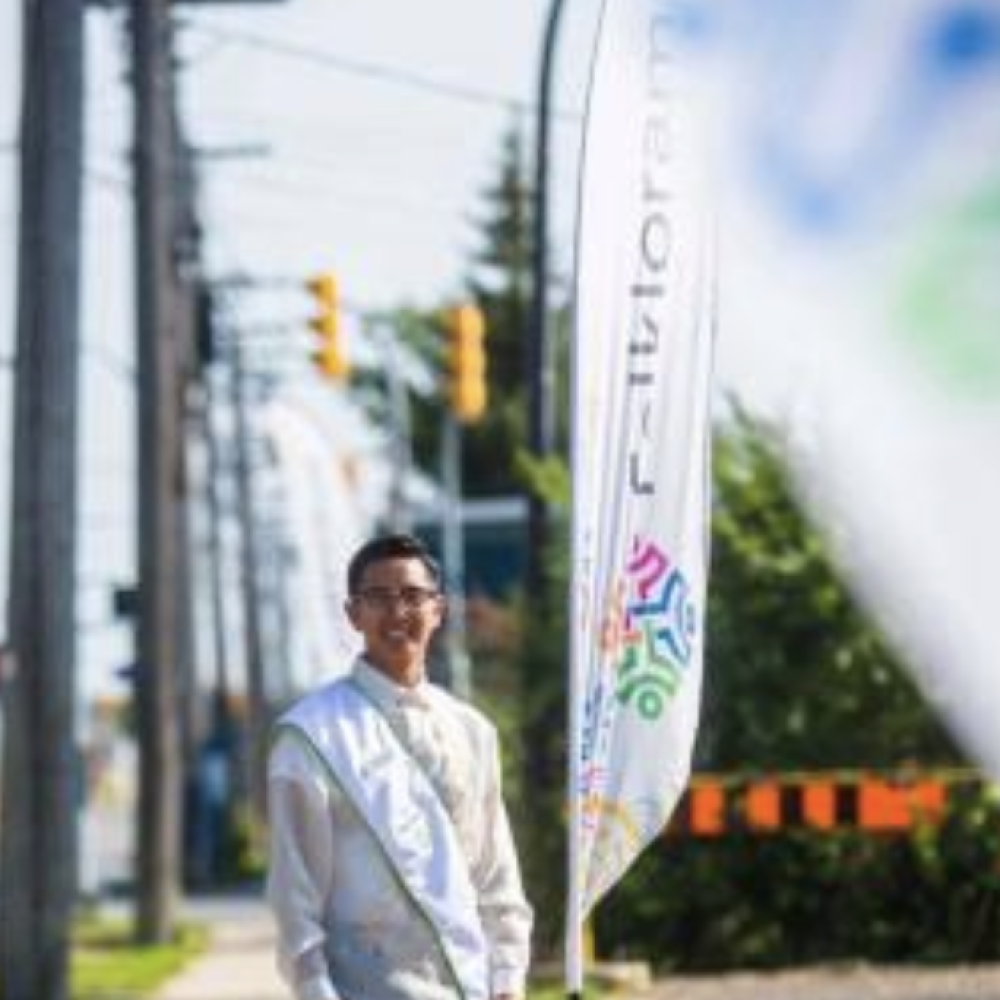 Joseph Orobia standing in formal attire near Folklorama banners